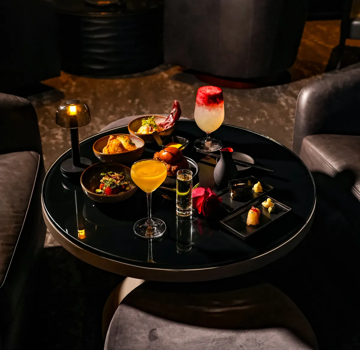 A lounge table set with cocktails and bites beside the club chairs