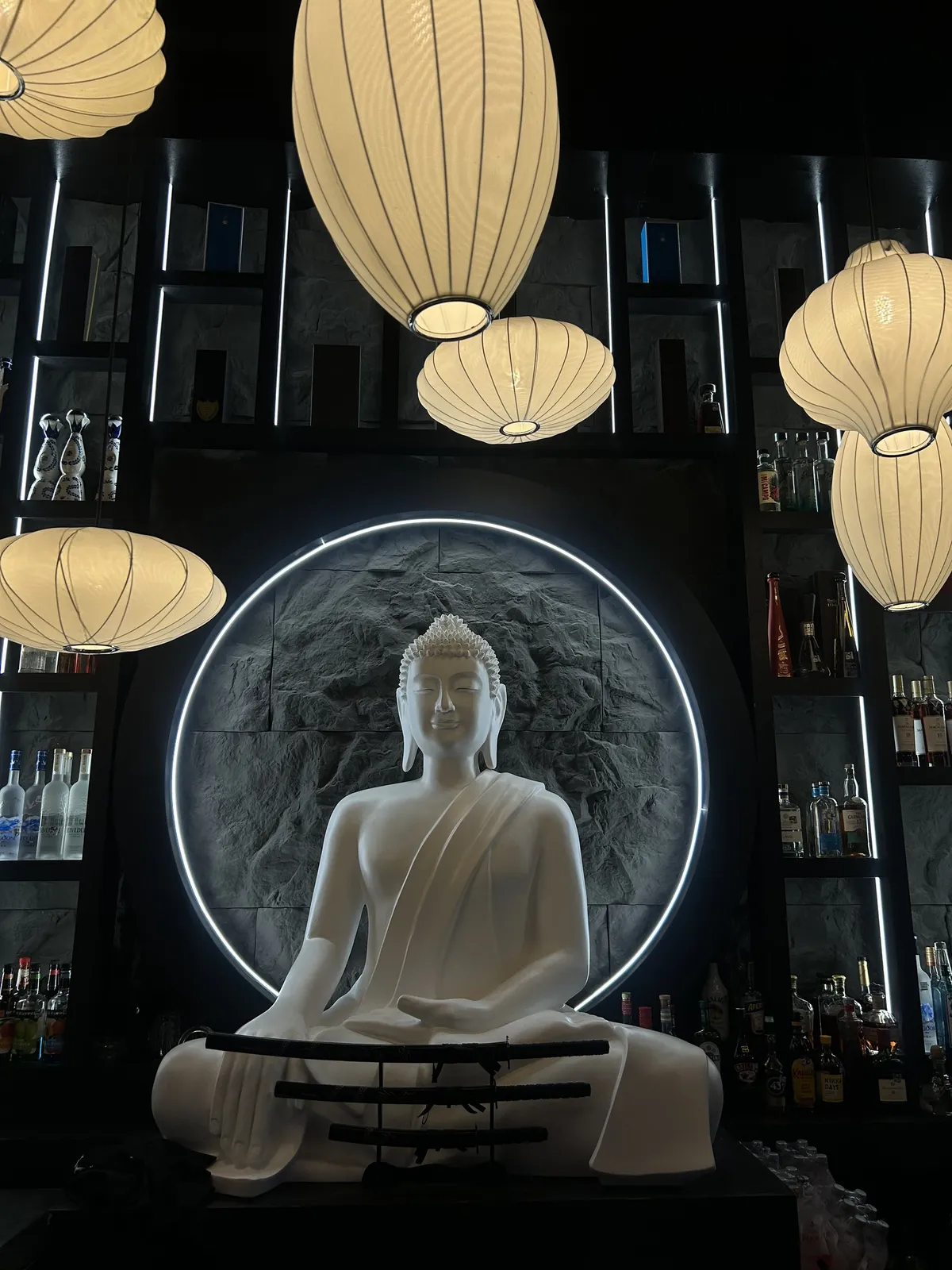 The bar at MOUSAI lit by lanterns beneath its Buddha sculpture