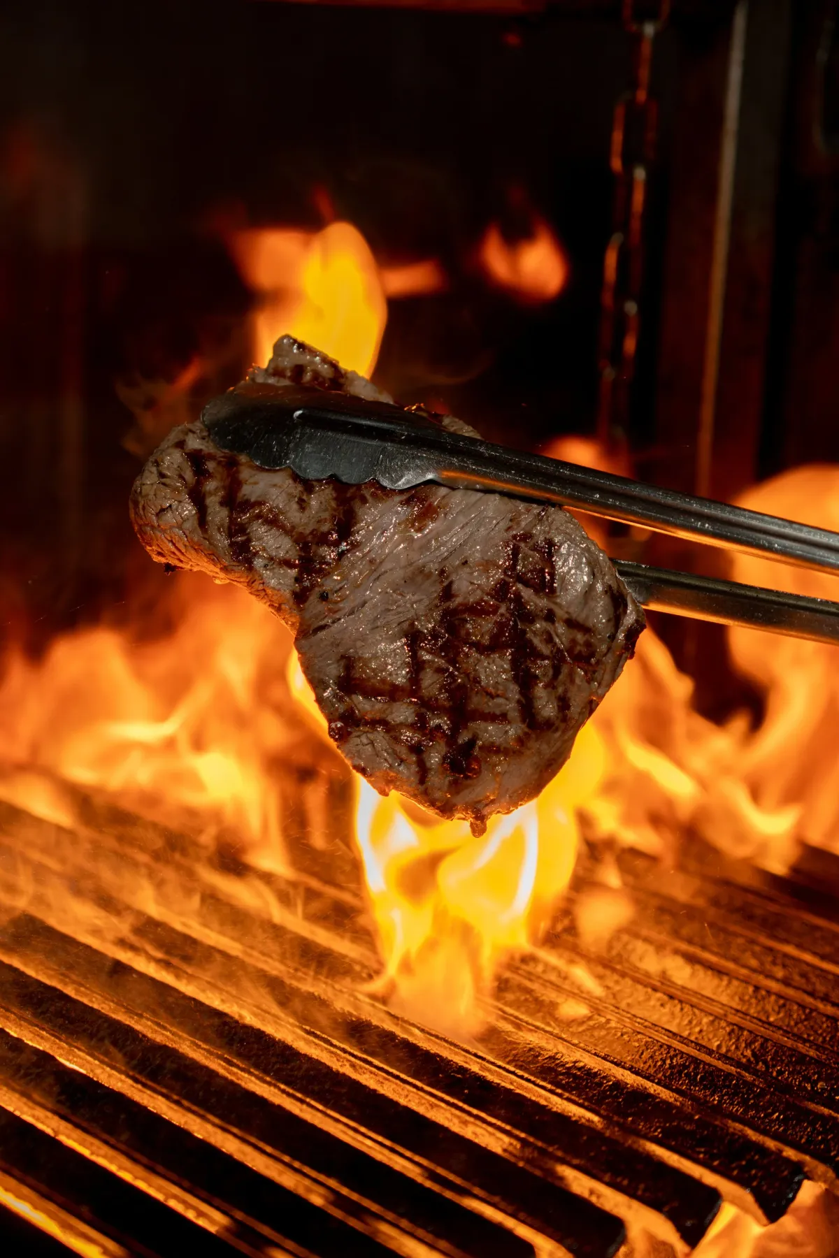 A steak lifted from the mesquite flames with tongs