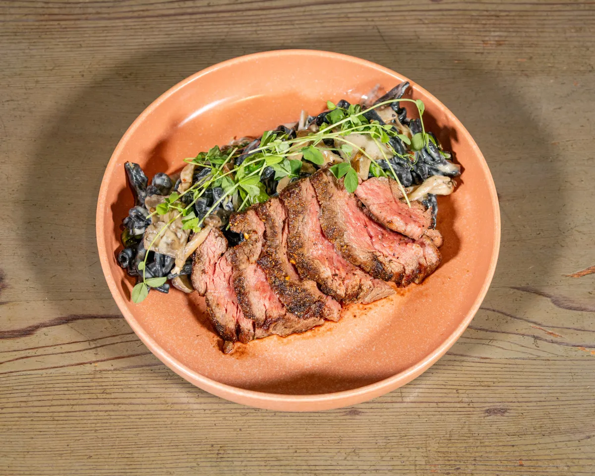 Sliced grilled steak over squid-ink pasta