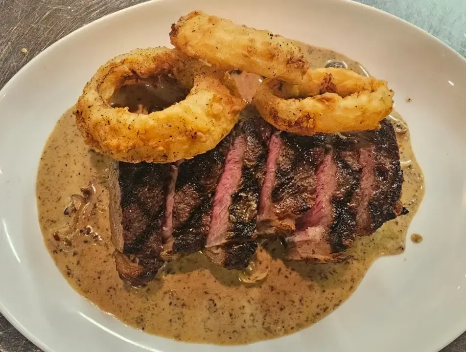 NY strip with crispy onion rings in peppercorn sauce